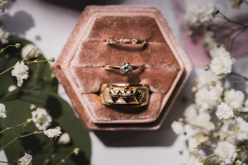 Catholic wedding bands sit in a pink ring box with flowers.